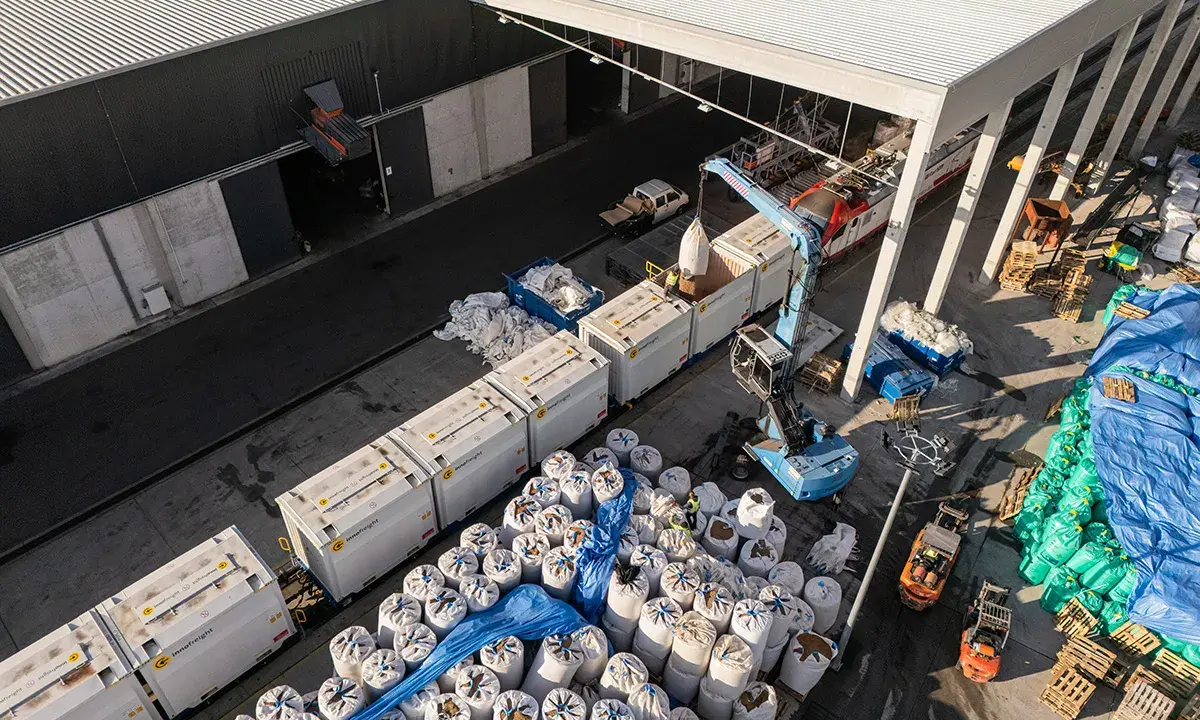 Tabor kolejowy i ciężarówki rozładowują worki z materiałem. To przykład logistyki i transportu.