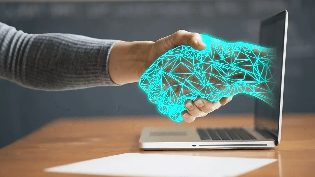 Dłoń wychodząca z laptopa, uścisk dłoni z cyfrową siatką. Ulga na powrót, gdy technologia łączy światy.