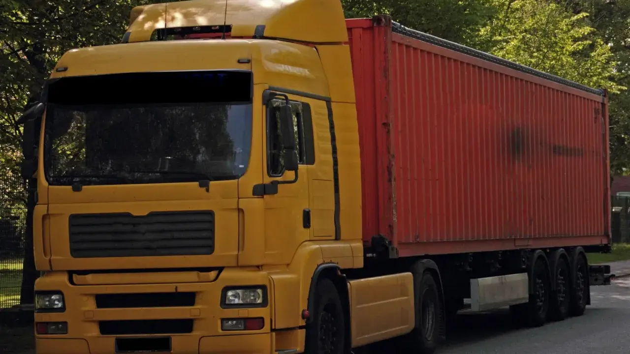 Żółta ciężarówka z czerwonym kontenerem, to pojazd drogowy bez silnika, gotowy do transportu.