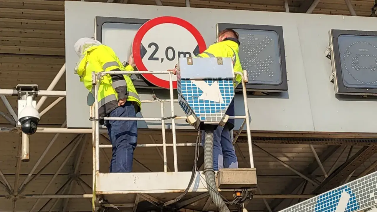 Dwóch pracowników na podnośniku montuje znak drogowy. Czy to część systemu etoll?