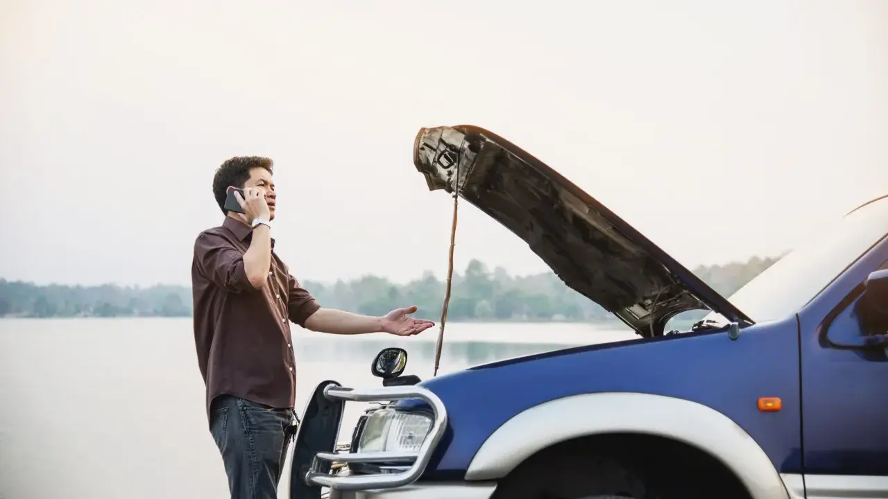 Mężczyzna z otwartą maską auta dzwoni po pomoc. Czy można holować auto bez przeglądu?