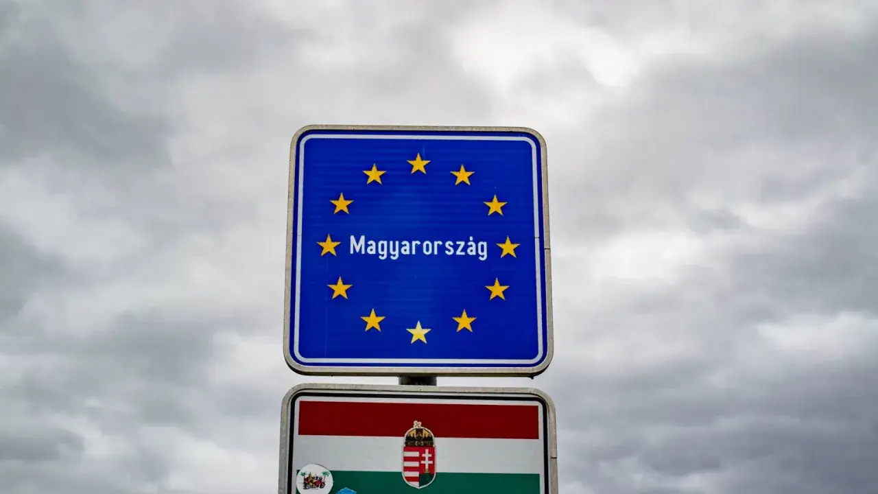 Znak graniczny z napisem "Magyarország" (Węgry) i flagą Węgier. W tle pochmurne niebo.