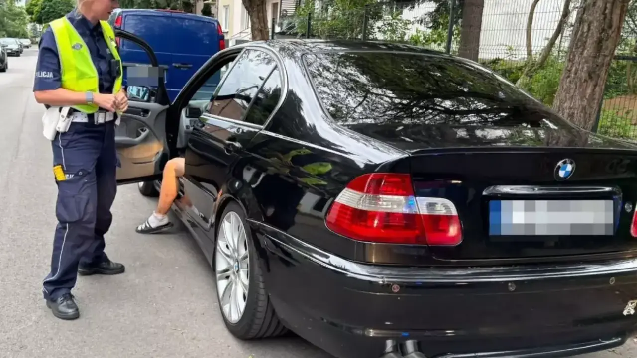 Policjantka zatrzymała kierowcę czarnego BMW. Kierowca wysiada z auta, prawdopodobnie czeka go więzienie za przekroczenie prędkości.