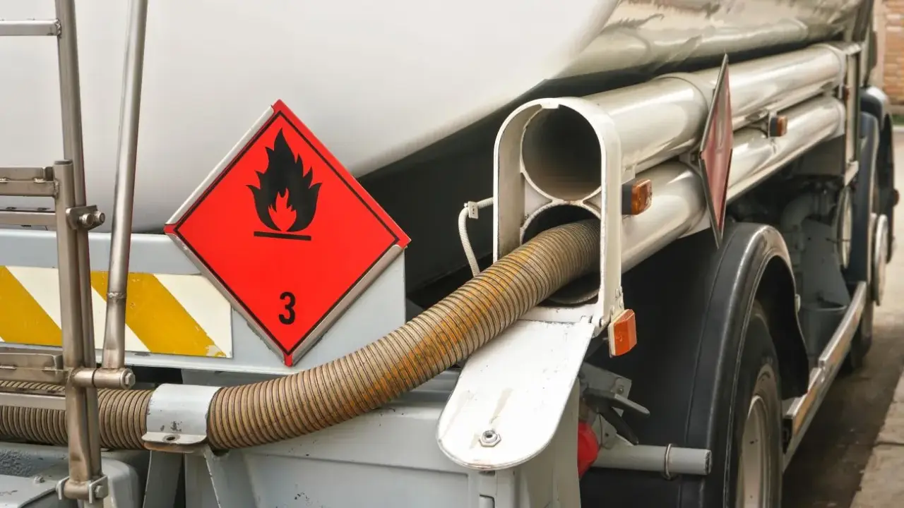 Zbliżenie na cysternę z oznaczeniem transportu towarów niebezpiecznych (płonący płomień, cyfra 3). Widoczny wąż do rozładunku.