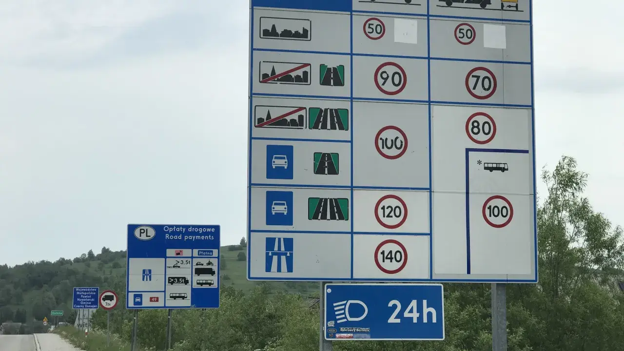 Znaki drogowe informują o opłatach i dopuszczalnych predkosci na drodze. Widoczne są ograniczenia prędkości dla różnych pojazdów.