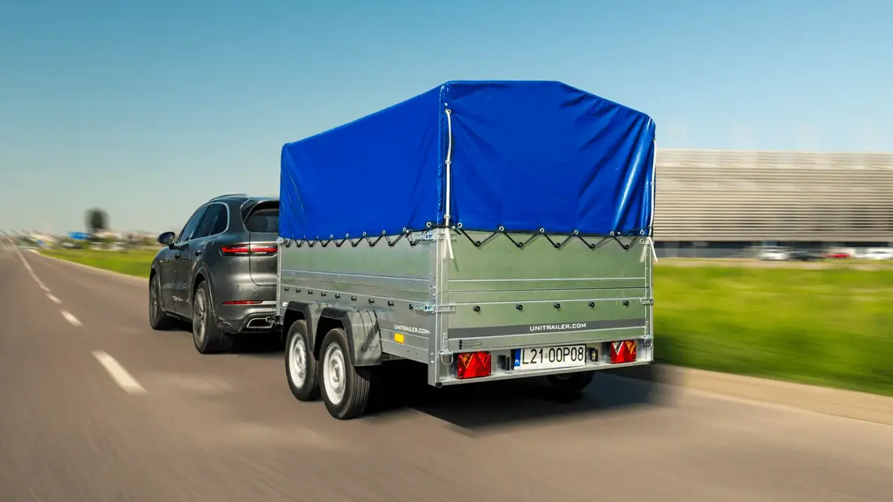 Ciemnoszary SUV ciągnie przyczepę z niebieską plandeką. Czy przyczepa to pojazd? Tak, gdy jest ciągnięta przez samochód.