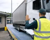 Pracownik w kamizelce odblaskowej zatrzymuje ręką ciężarówkę na wadze, by sprawdzić jej masę i przestrzeganie ograniczeń tonażowych.