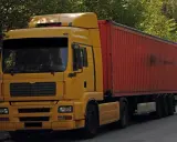 Żółta ciężarówka z czerwonym kontenerem, to pojazd drogowy bez silnika, gotowy do transportu.