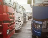 Rzędy ciężarówek, czerwona, biała i niebieska. Nowoczesna telematyka co to? Optymalizacja logistyki.