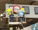 Dwóch pracowników na podnośniku montuje znak drogowy. Czy to część systemu etoll?