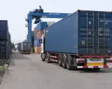 Ciężarówka z kontenerem na pace, jakby na piggy back, jedzie przez terminal kontenerowy pod suwnicą PKP Cargo.