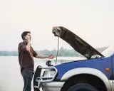 Mężczyzna z otwartą maską auta dzwoni po pomoc. Czy można holować auto bez przeglądu?