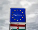 Znak graniczny z napisem "Magyarország" (Węgry) i flagą Węgier. W tle pochmurne niebo.