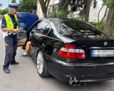 Policjantka zatrzymała kierowcę czarnego BMW. Kierowca wysiada z auta, prawdopodobnie czeka go więzienie za przekroczenie prędkości.