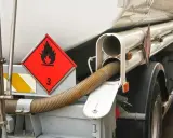 Zbliżenie na cysternę z oznaczeniem transportu towarów niebezpiecznych (płonący płomień, cyfra 3). Widoczny wąż do rozładunku.