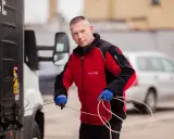 Mężczyzna w czerwonej kurtce z logo Visline, w niebieskich rękawicach, trzyma sznur przyczepiony do naczepy ciężarówki. Czy to ldm co to za usługa?