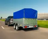 Ciemnoszary SUV ciągnie przyczepę z niebieską plandeką. Czy przyczepa to pojazd? Tak, gdy jest ciągnięta przez samochód.