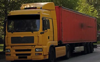Żółta ciężarówka z czerwonym kontenerem, to pojazd drogowy bez silnika, gotowy do transportu.