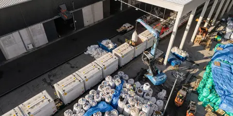 Tabor kolejowy i ciężarówki rozładowują worki z materiałem. To przykład logistyki i transportu.