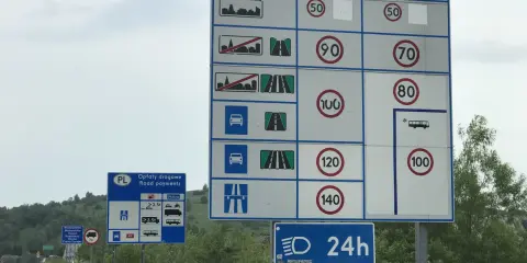 Znaki drogowe informują o opłatach i dopuszczalnych predkosci na drodze. Widoczne są ograniczenia prędkości dla różnych pojazdów.