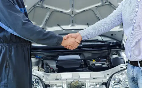 Mechanik i klient ściskają sobie dłonie przy otwartej masce samochodu. To pierwszy przegląd w kraju, symbol zaufania i dobrej współpracy.