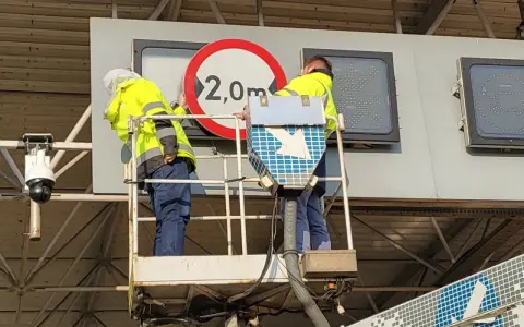Dwóch pracowników na podnośniku montuje znak drogowy. Czy to część systemu etoll?