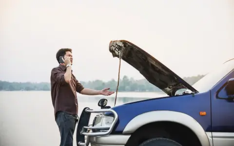 Mężczyzna z otwartą maską auta dzwoni po pomoc. Czy można holować auto bez przeglądu?