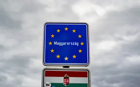 Znak graniczny z napisem "Magyarország" (Węgry) i flagą Węgier. W tle pochmurne niebo.