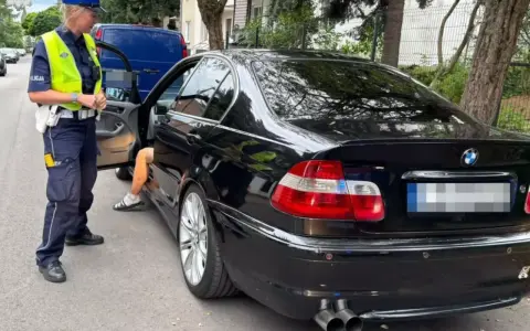 Policjantka zatrzymała kierowcę czarnego BMW. Kierowca wysiada z auta, prawdopodobnie czeka go więzienie za przekroczenie prędkości.