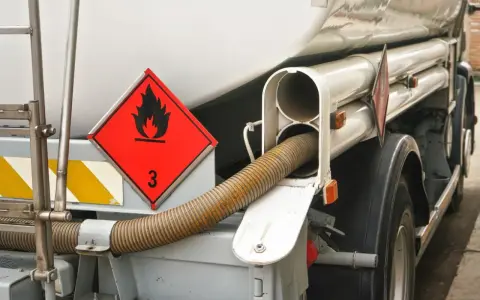 Zbliżenie na cysternę z oznaczeniem transportu towarów niebezpiecznych (płonący płomień, cyfra 3). Widoczny wąż do rozładunku.