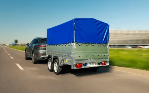 Ciemnoszary SUV ciągnie przyczepę z niebieską plandeką. Czy przyczepa to pojazd? Tak, gdy jest ciągnięta przez samochód.