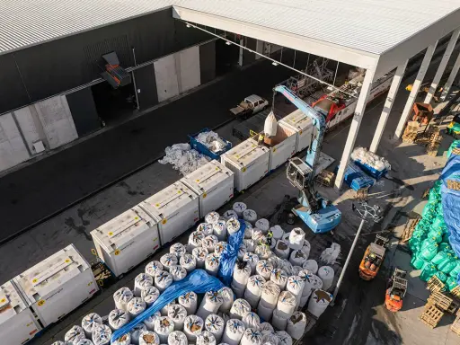 Tabor kolejowy i ciężarówki rozładowują worki z materiałem. To przykład logistyki i transportu.