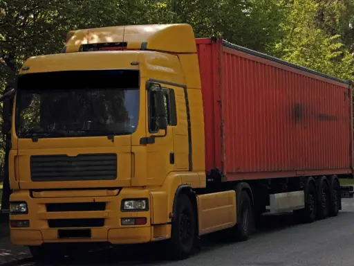 Żółta ciężarówka z czerwonym kontenerem, to pojazd drogowy bez silnika, gotowy do transportu.