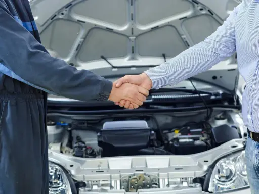 Mechanik i klient ściskają sobie dłonie przy otwartej masce samochodu. To pierwszy przegląd w kraju, symbol zaufania i dobrej współpracy.