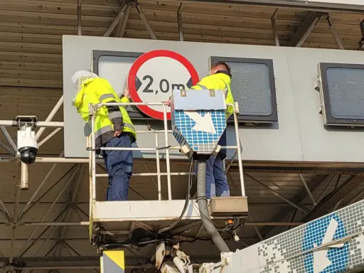 Dwóch pracowników na podnośniku montuje znak drogowy. Czy to część systemu etoll?
