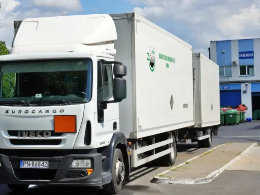 Biała ciężarówka Iveco z naczepą, gotowa do transportu odpadów niebezpiecznych. Na naczepie logo firmy "Zakład Utylizacji Odpadów Sp. z o.o. Konin".