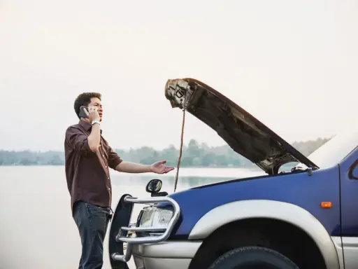 Mężczyzna z otwartą maską auta dzwoni po pomoc. Czy można holować auto bez przeglądu?