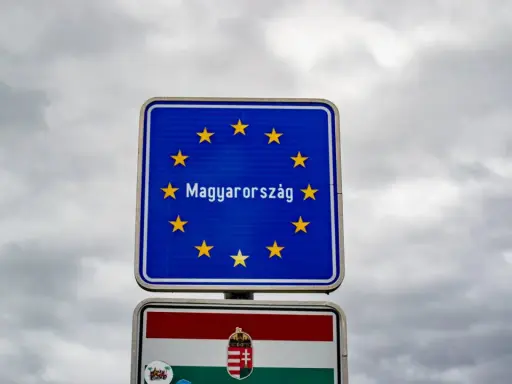 Znak graniczny z napisem "Magyarország" (Węgry) i flagą Węgier. W tle pochmurne niebo.