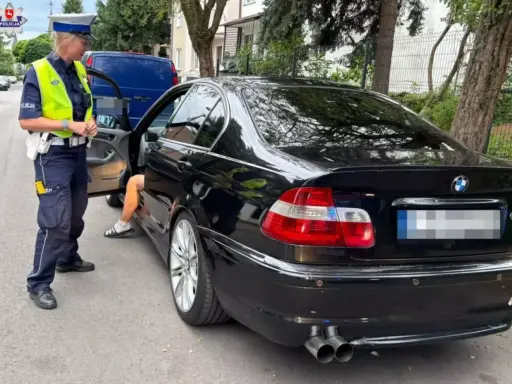 Policjantka zatrzymała kierowcę czarnego BMW. Kierowca wysiada z auta, prawdopodobnie czeka go więzienie za przekroczenie prędkości.