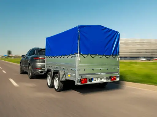 Ciemnoszary SUV ciągnie przyczepę z niebieską plandeką. Czy przyczepa to pojazd? Tak, gdy jest ciągnięta przez samochód.