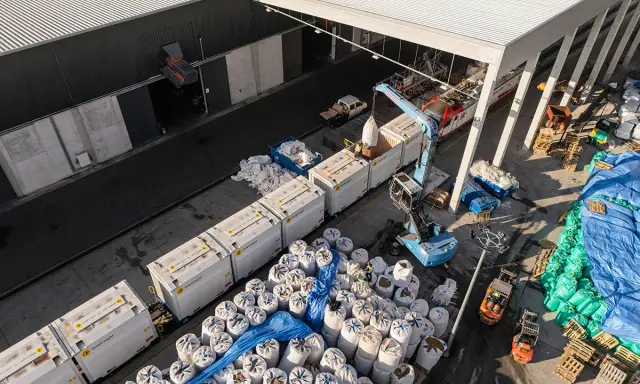 Tabor kolejowy i ciężarówki rozładowują worki z materiałem. To przykład logistyki i transportu.