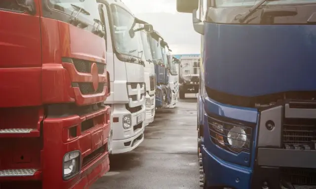 Rzędy ciężarówek, czerwona, biała i niebieska. Nowoczesna telematyka co to? Optymalizacja logistyki.