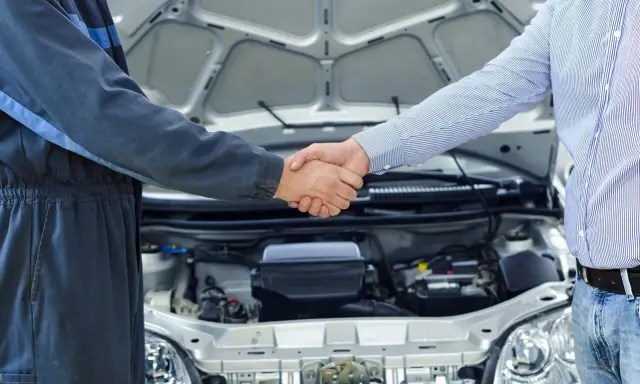 Mechanik i klient ściskają sobie dłonie przy otwartej masce samochodu. To pierwszy przegląd w kraju, symbol zaufania i dobrej współpracy.