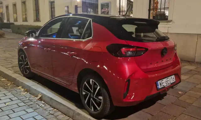 Czerwony samochód firmowy Opel Corsa, zaparkowany na ulicy. Czy to znak zawieszenia działalności?
