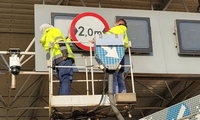 Dwóch pracowników na podnośniku montuje znak drogowy. Czy to część systemu etoll?
