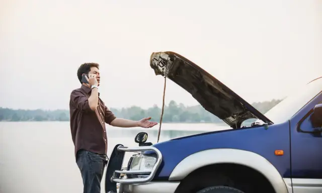 Mężczyzna z otwartą maską auta dzwoni po pomoc. Czy można holować auto bez przeglądu?