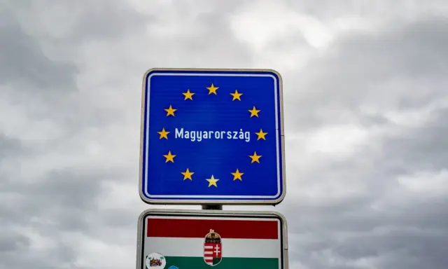 Znak graniczny z napisem "Magyarország" (Węgry) i flagą Węgier. W tle pochmurne niebo.