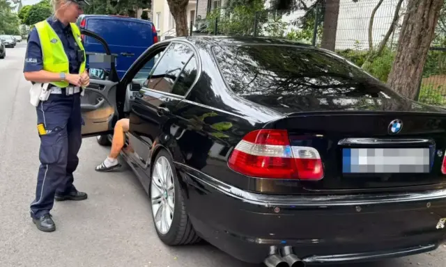 Policjantka zatrzymała kierowcę czarnego BMW. Kierowca wysiada z auta, prawdopodobnie czeka go więzienie za przekroczenie prędkości.
