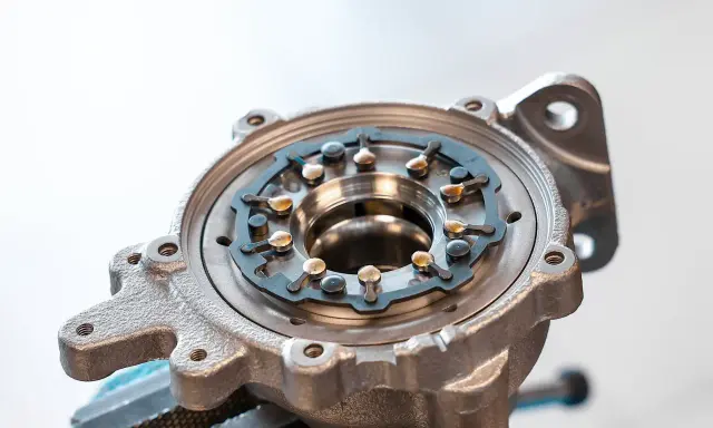 Metalowa obudowa turbosprężarki ze zmienną geometrią, z widocznymi łopatkami i mechanizmem regulacji.
