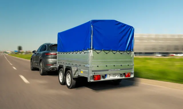 Ciemnoszary SUV ciągnie przyczepę z niebieską plandeką. Czy przyczepa to pojazd? Tak, gdy jest ciągnięta przez samochód.